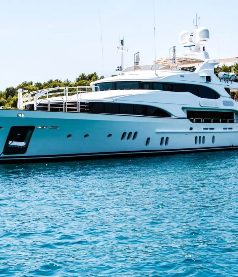 Large white luxury yacht cruising calm blue waters near a forested coastline.