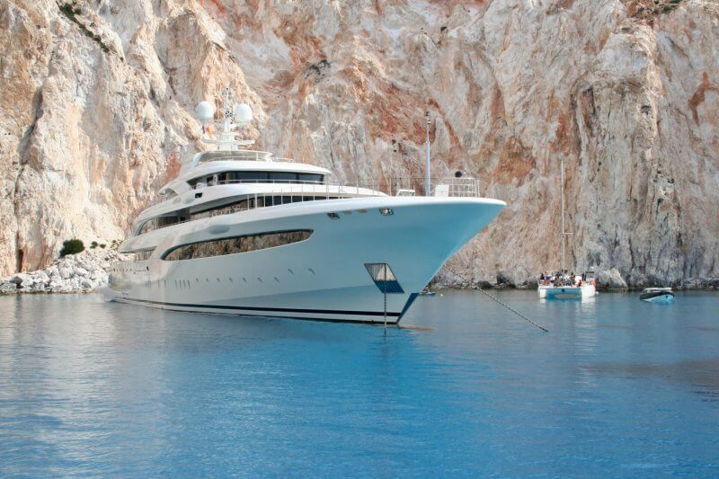 Large luxury yacht anchored in a secluded cove with towering limestone cliffs.