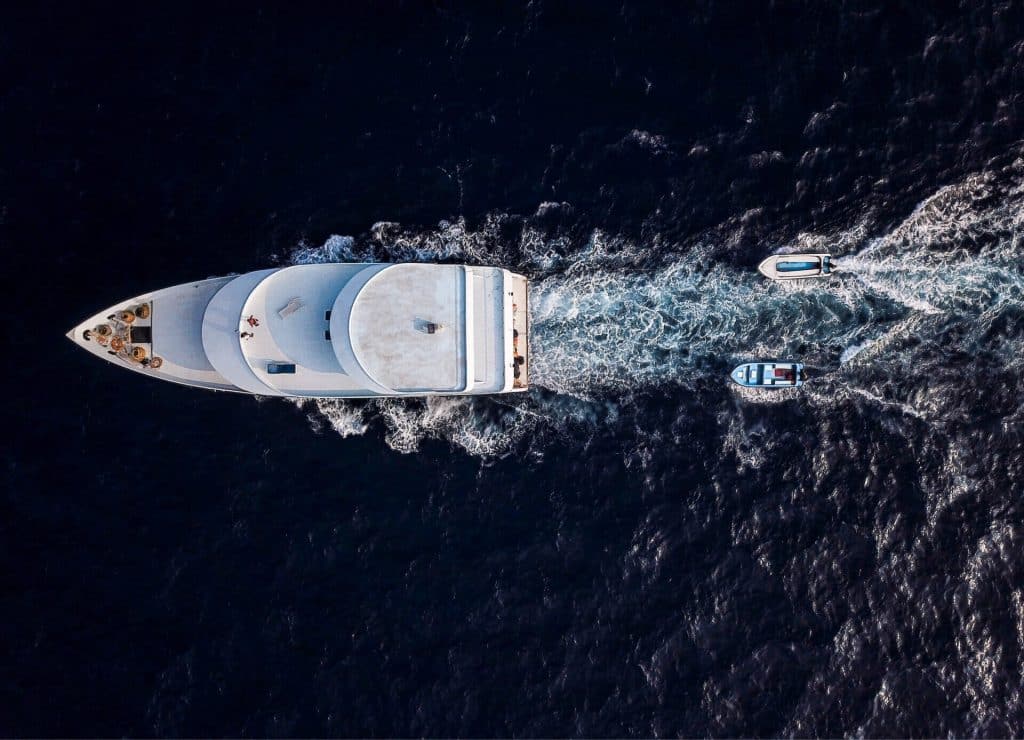 Aerial view of a large white superyacht cruising, with two tenders trailing behind.